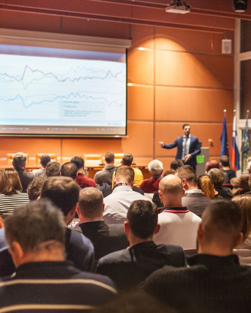 A speaker presents data trends to a seated audience in a conference room.