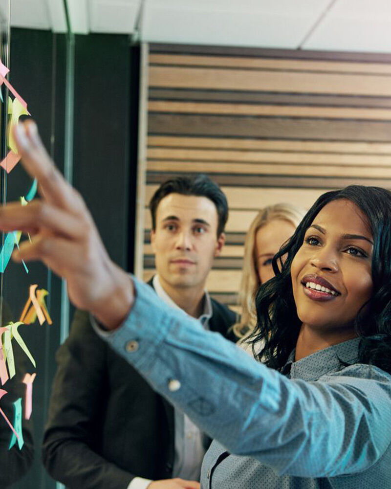 A woman points while a group listens attentively in a modern office.