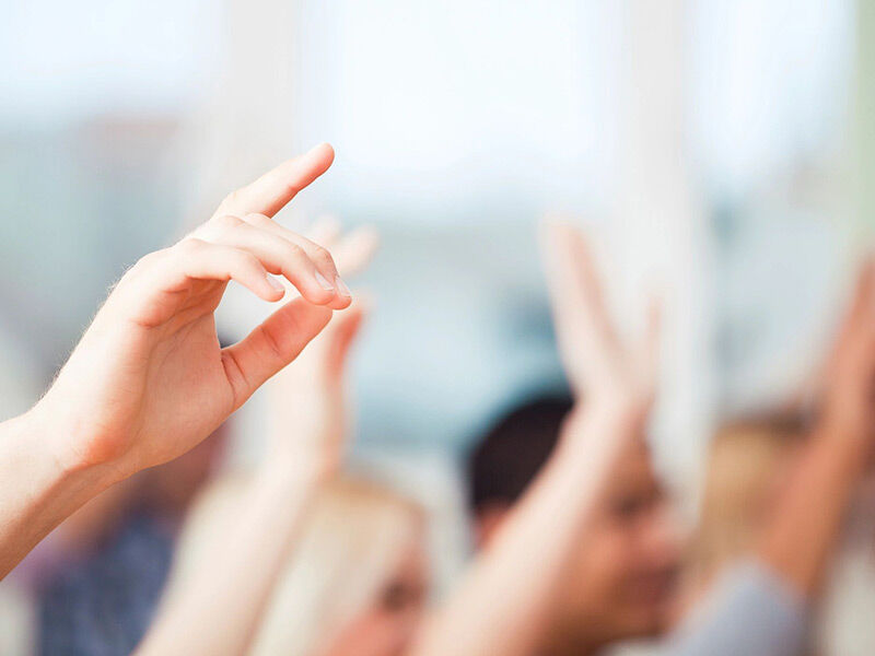 Raised hands in a blurred background, signaling participation or voting.